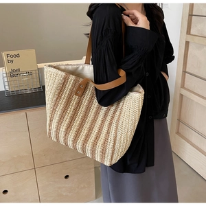 Detail of a large woven straw tote bag with brown leather straps shown on a model