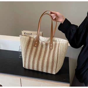 Detail of the woven straw tote bag featuring brown leather straps and metal rivets