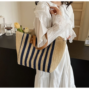 Detail of striped straw tote bag with brown PU leather handles and metal rivet reinforcement