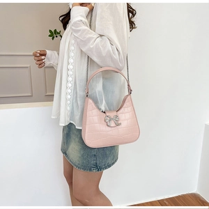 Pink faux leather shoulder bag with crocodile pattern and rhinestone bow detail