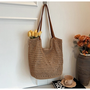 French style woven straw shoulder bag with leather straps hanging on a white wall