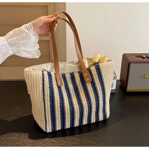 Detail of the woven straw tote bag with beige and blue vertical stripes and leather handles