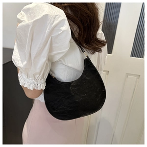 Detail view of black crescent moon shoulder bag with pleated faux leather texture on model