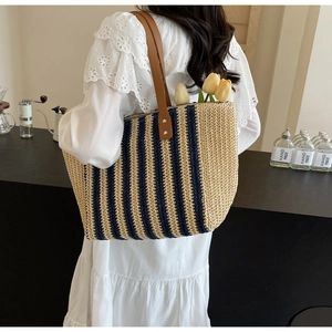 Straw tote bag with blue stripes and brown leather straps shown on a model's shoulder