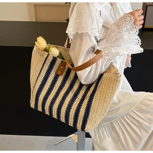 Detail of striped straw tote bag featuring blue stripes and brown leather handles with rivets