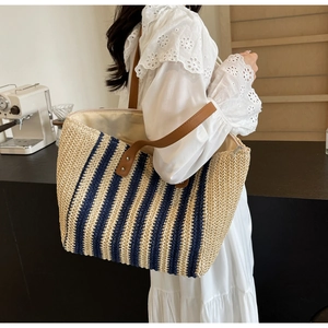 Detail view of woven straw tote bag with navy stripes and brown leather shoulder straps