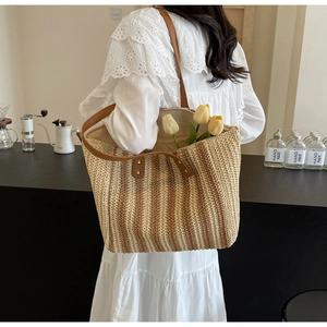 Detailed view of woven straw tote bag texture and brown leather strap with metal rivets
