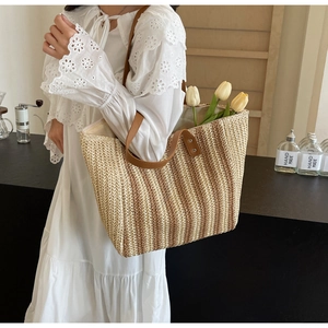 Close-up of woven straw tote bag featuring vertical brown stripes and leather handles