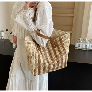 Detail of hand-woven straw tote bag showing beige stripes and brown leather handles
