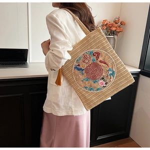 Detail of a straw tote bag featuring traditional Chinese embroidery and a yellow tassel