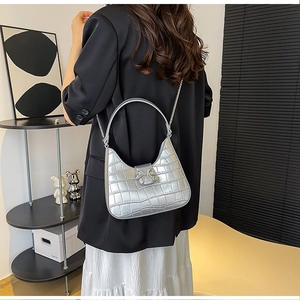 Close-up of silver crocodile embossed handbag with rhinestone bow buckle and metal chain