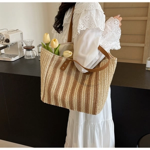 Detail of a large woven straw beach tote bag with brown leather straps near a coffee shop