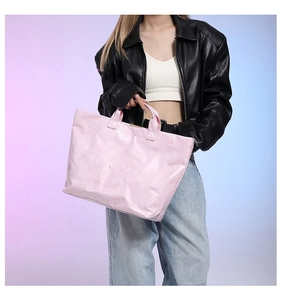 Pink metallic tote bag with white TOTE BAG slogan held by a model in a leather jacket
