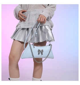 Detail of light blue PU leather bag featuring a silver metal bow and chain strap