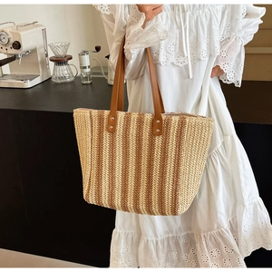 Detail of a large capacity straw tote bag with vertical stripes and leather handles