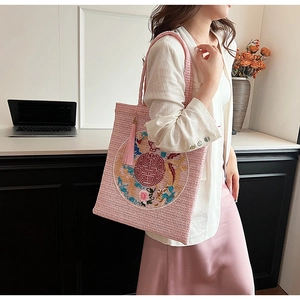 Close-up of pink straw woven tote bag featuring dragon phoenix embroidery and tassel charm