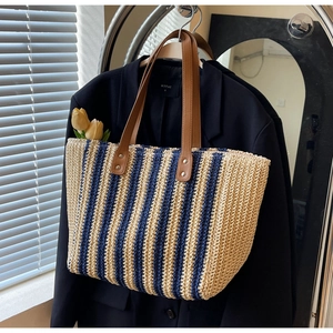 Detail of woven straw tote bag with blue stripes and premium brown leather handles