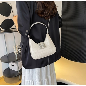 Detail of hobo bag in cream crocodile pattern with rhinestone bow and silver chain strap