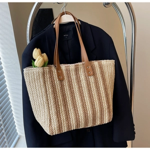 Close-up of woven straw tote bag with brown leather straps and silver metal rivets