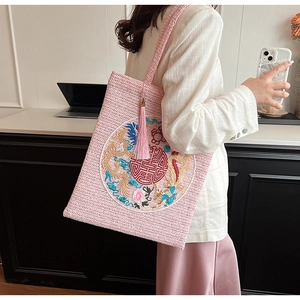 Detailed embroidery of a dragon and floral pattern on a pink woven straw tote bag