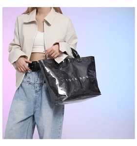 Fashionable black glossy tote bag with white text held by a model in casual outfit