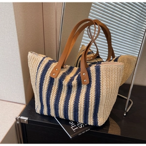 Detailed macro view of large striped straw tote bag featuring brown PU leather handles