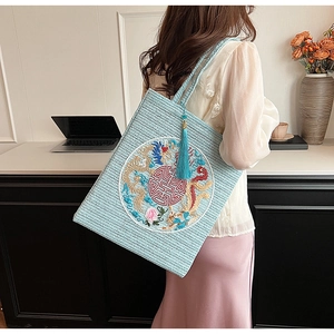 Detail of light blue straw tote bag with golden dragon embroidery and decorative tassel