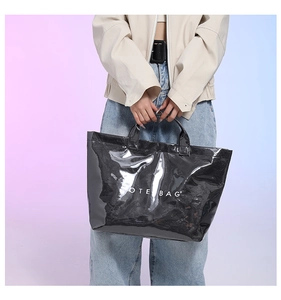 Detail of a black glossy tote bag featuring white TOTE BAG text held by a model