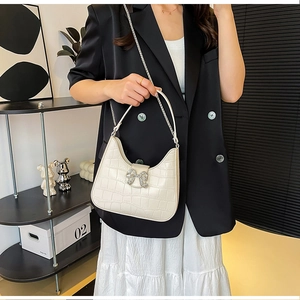 Detail of cream PU leather bag with crocodile texture and rhinestone bow buckle