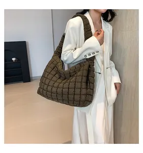 Detail of olive green quilted cloud tote bag worn by a model in a white suit