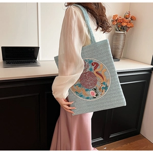 Detail view of light blue woven tote bag with traditional Chinese embroidery on a model