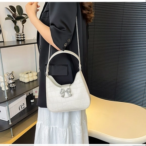 Detail of white crocodile texture bag featuring a sparkling silver rhinestone bow clasp