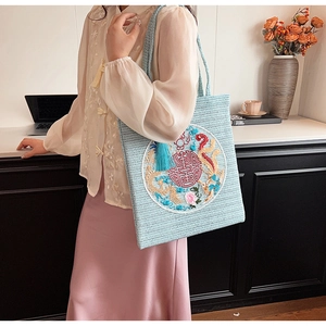Close-up of light blue straw tote bag with dragon phoenix embroidery and fringe detail
