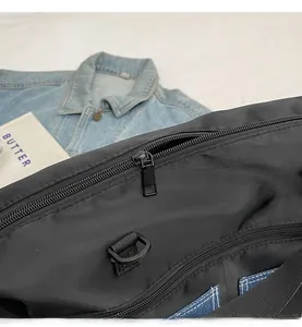 Detail of smooth metal zipper and D-ring on black nylon crossbody bag with denim trim