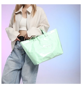 Detail of mint green crinkled tote bag with embossed logo worn by fashion model