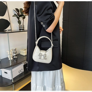 Detail showing white croc-embossed handbag with sparkling rhinestone bow and chain strap