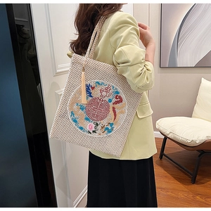 Detail of cream woven tote bag featuring dragon embroidery and yellow tassel charm