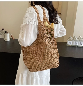 Detail of a brown woven straw tote bag with large hollow mesh and floral decoration