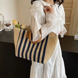 Large navy striped straw tote bag with brown leather handles and a zipper for beach vacations