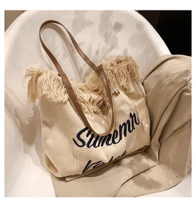 Détail du cabas tissé blanc cassé avec franges et broderie Summer posé sur une chaise