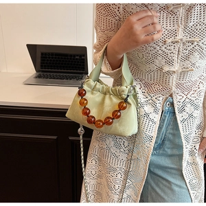 Detail of light green ruched pouch bag featuring retro amber bead handle and chain strap