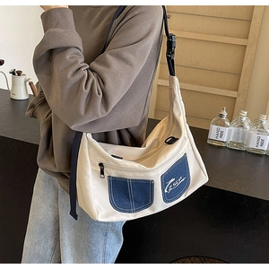 Detail of white canvas crossbody bag with blue denim pockets and adjustable black strap