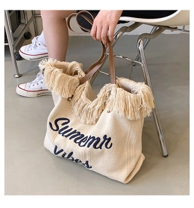 Détail du cabas tissé crème avec broderie Summer Vibes, franges et anses en cuir marron
