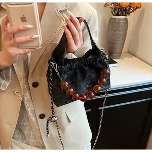 Detail of black drawstring crossbody bag with amber beads and metal chain strap