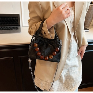 Detail of black pleated PU handbag with amber resin beads and silver chain strap