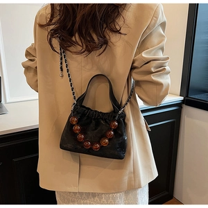 Detail view of black pleated PU handbag with amber beads and leather chain strap