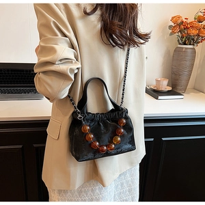 Close-up of black ruched PU leather handbag with amber beads and metal chain strap