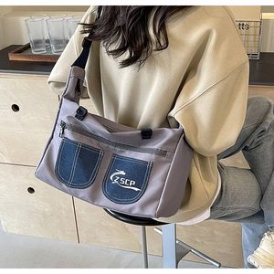 Detail of grey crossbody messenger bag with denim pockets and adjustable black strap