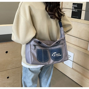 Detail view of a gray nylon messenger bag with blue denim pockets and a zip closure