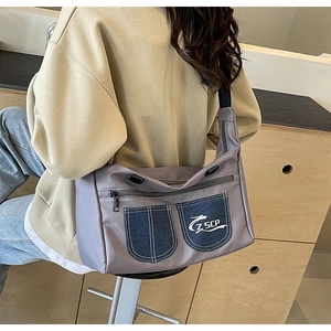 Detail view of a grey-purple nylon crossbody bag with denim pockets and wide black strap